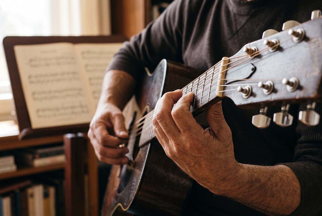 Beginner's fingers on a guitar fretboard with sheet music nearby, showing the tasks reading asks them to coordinate.