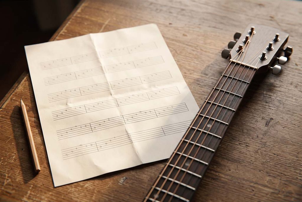 Six lines of guitar tablature beside an acoustic guitar fretboard on a wooden table.