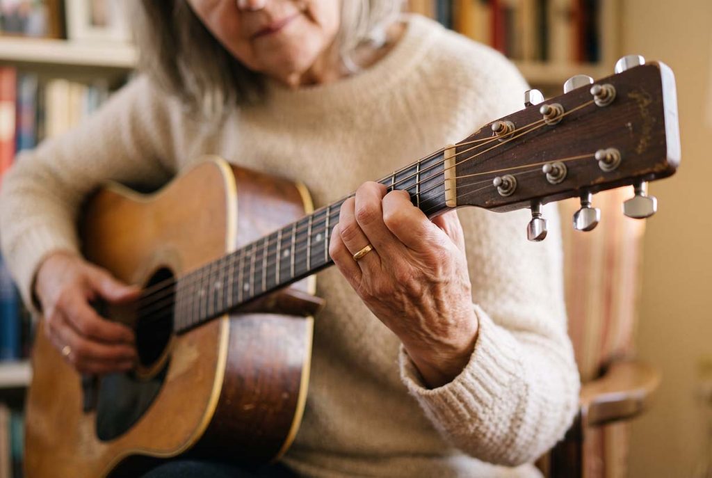 An older woman's fingertips on guitar strings during her return to playing and rebuilding hand conditioning.