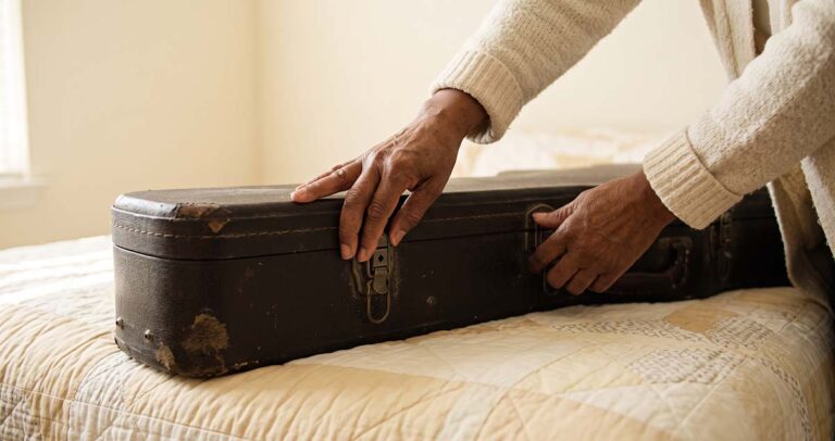 An older woman's hands opening a worn guitar case after years away from playing.